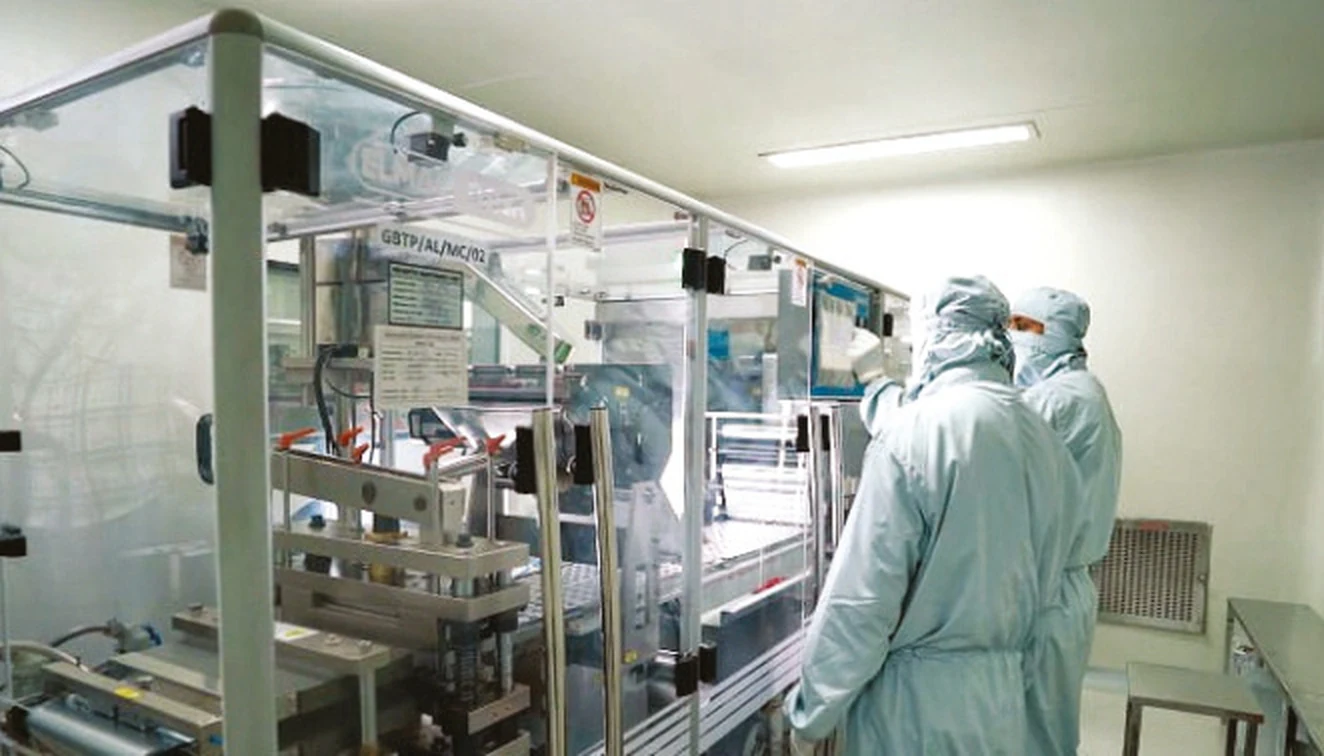 Operators in sterile gowning working an automated blister packing line inside a controlled cleanroom